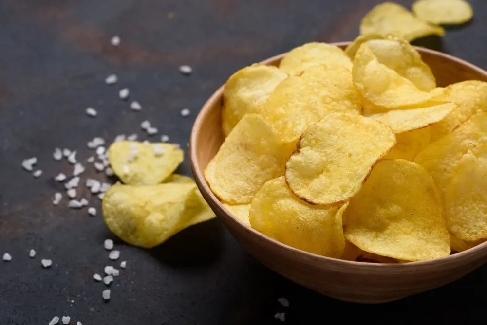 High angle view of bowl of potato chips with salt surrounding on table